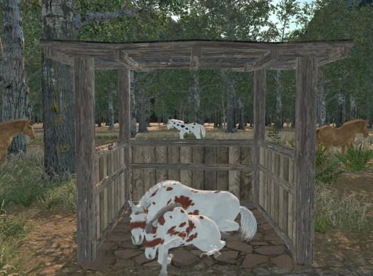 A wooden horse pen in a lush medieval forest setting with horses grazing nearby.
